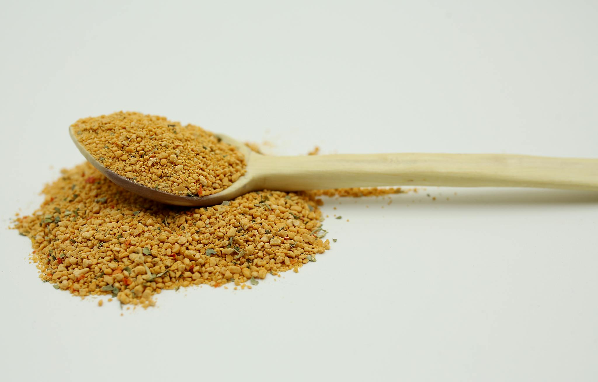 A wooden spoon filled with bee pollen granules on a white background, highlighting natural textures.